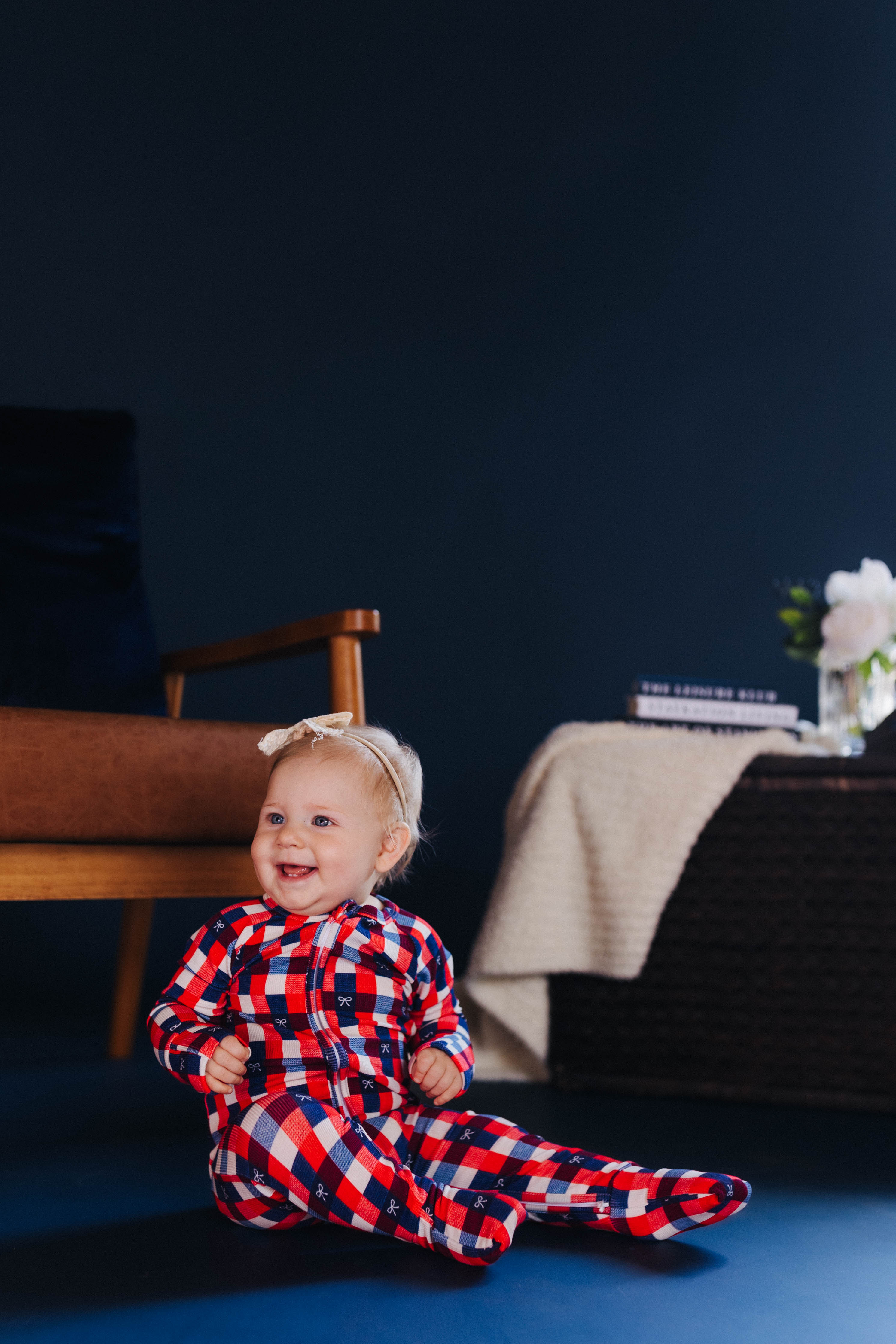 child smiling wearing red white and blue gingham onesie sitting