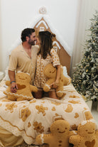 Couple sitting on a bed with gingerbread-themed decor, including a gingerbread house and tree.