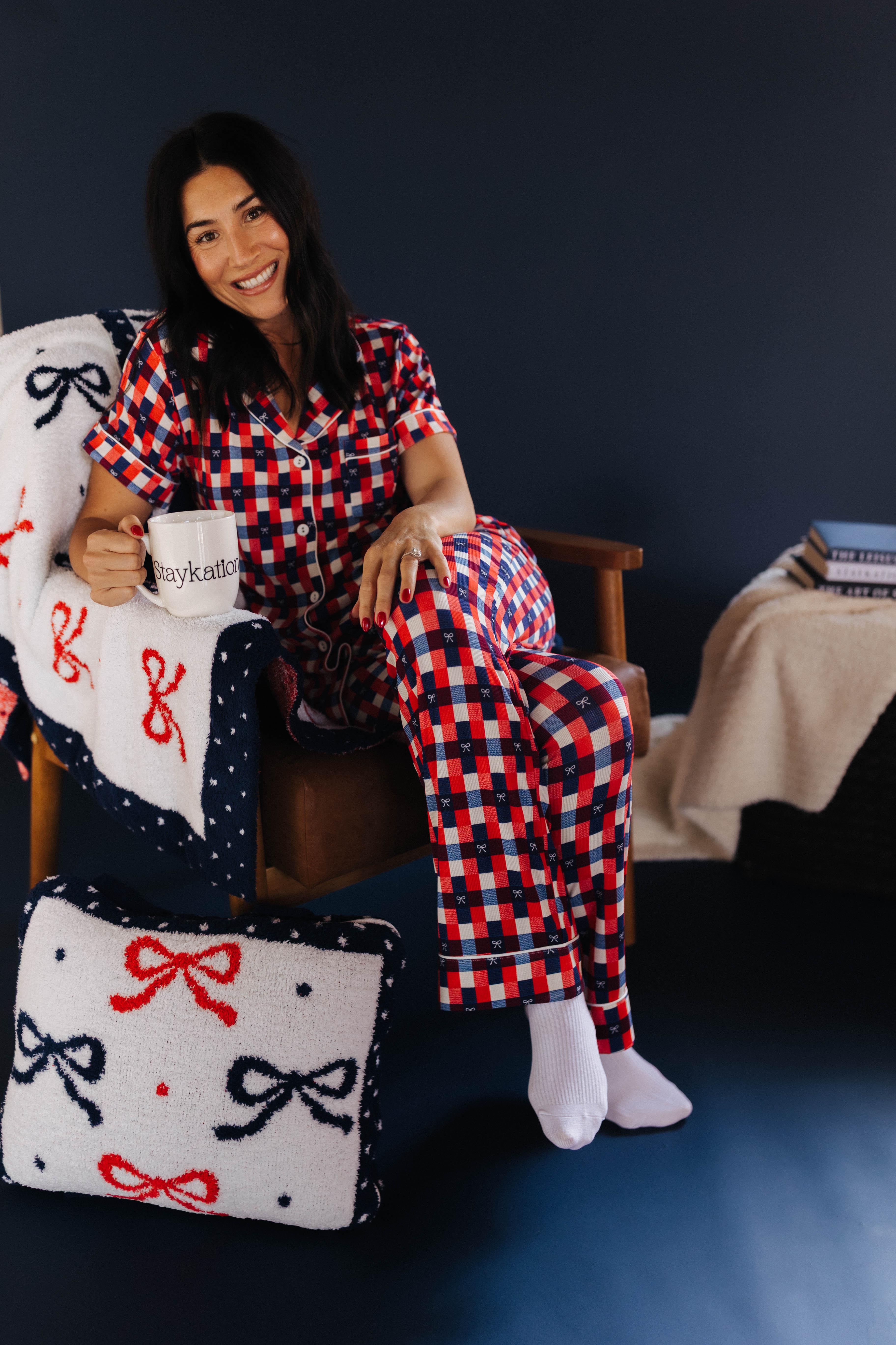 Woman in red and blue checkered pajama set sitting on a chair with a quillow featuring bows.