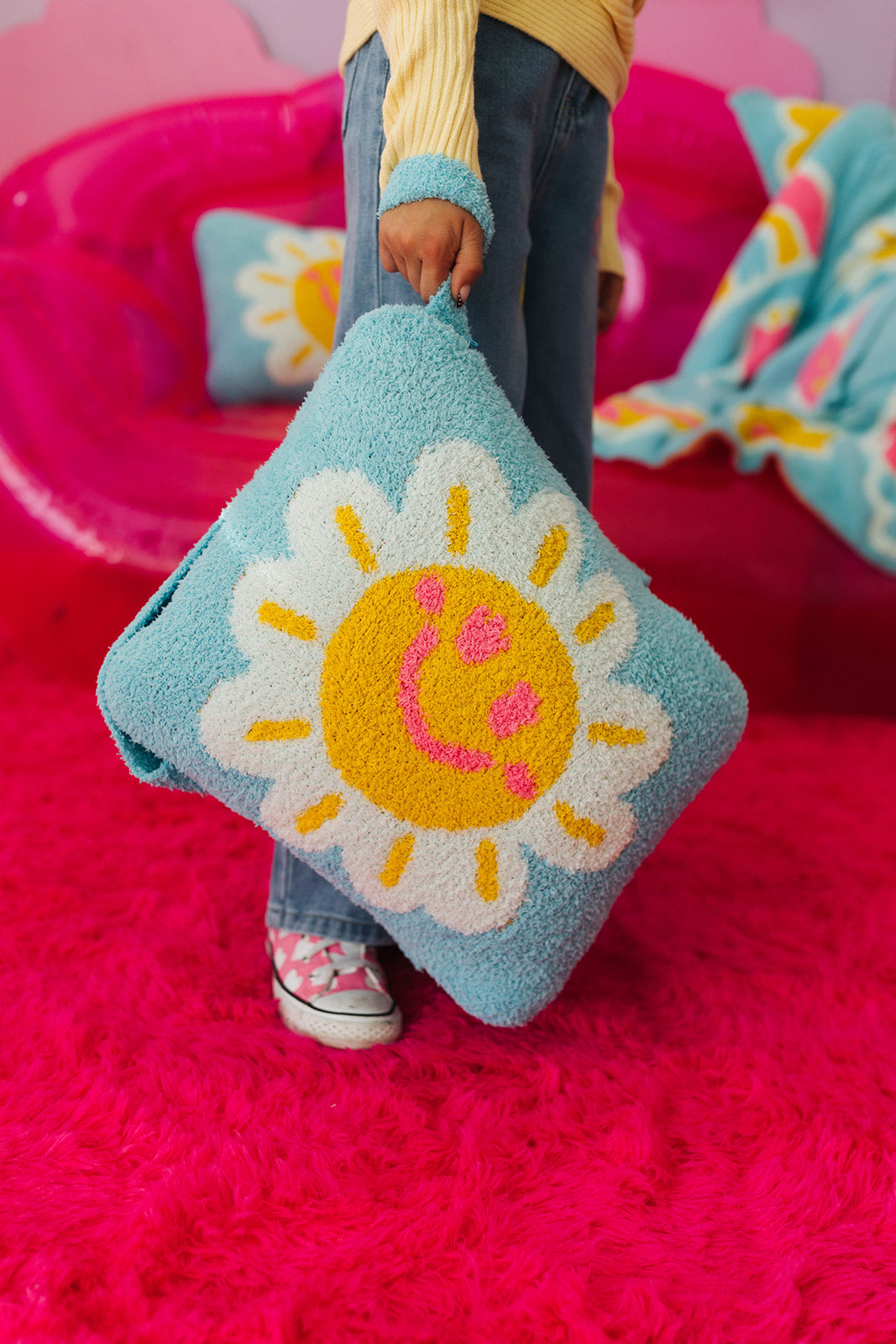 Person holding a blue pillow with a sun design on a pink background