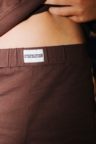 Close-up of a person wearing dark brown shorts with a white waistband label that reads 'STAYKATION'.
