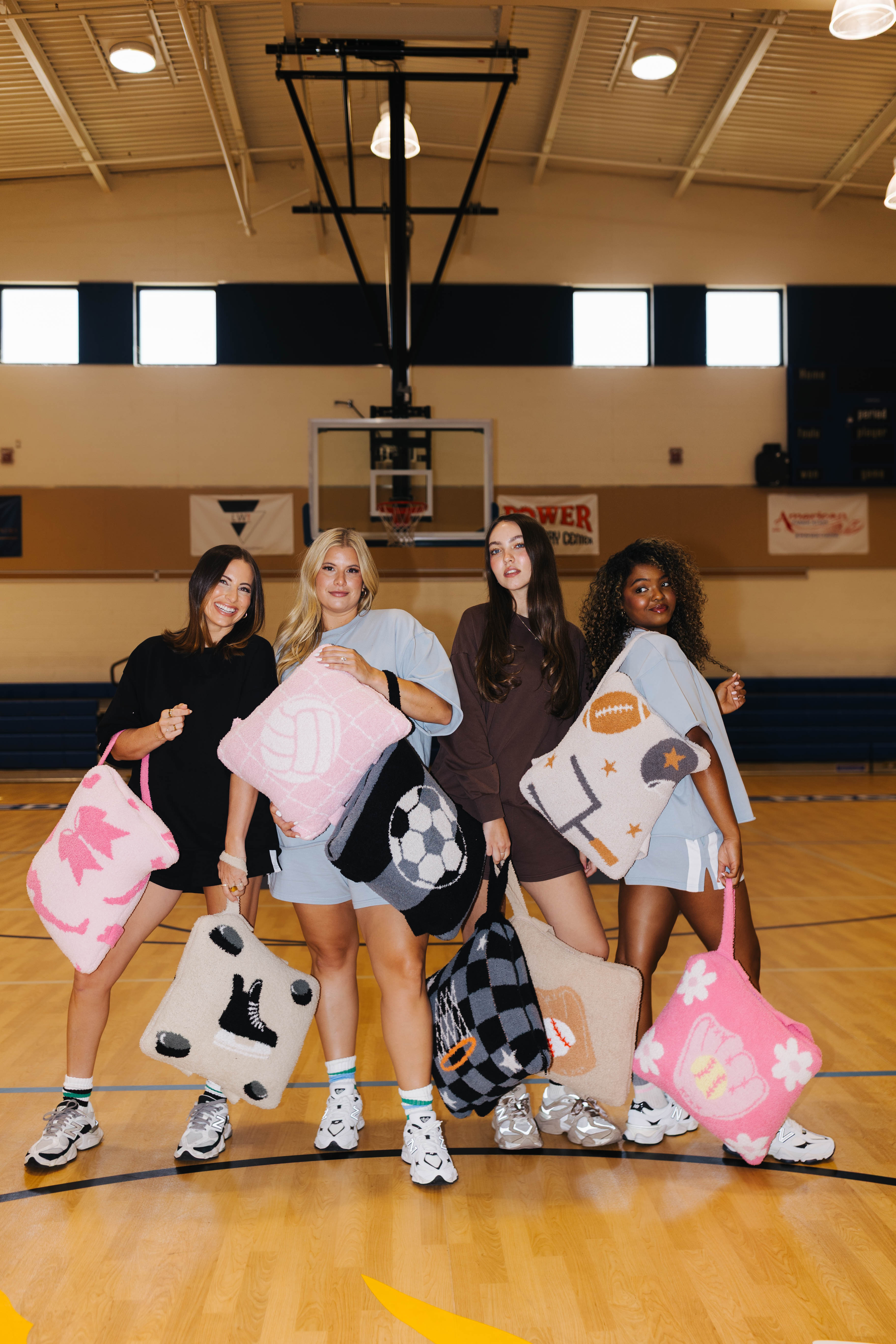 Four women standing on a school gymnasium basketball court holding various quillows