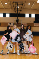 Four women standing on a school gymnasium basketball court holding various quillows.