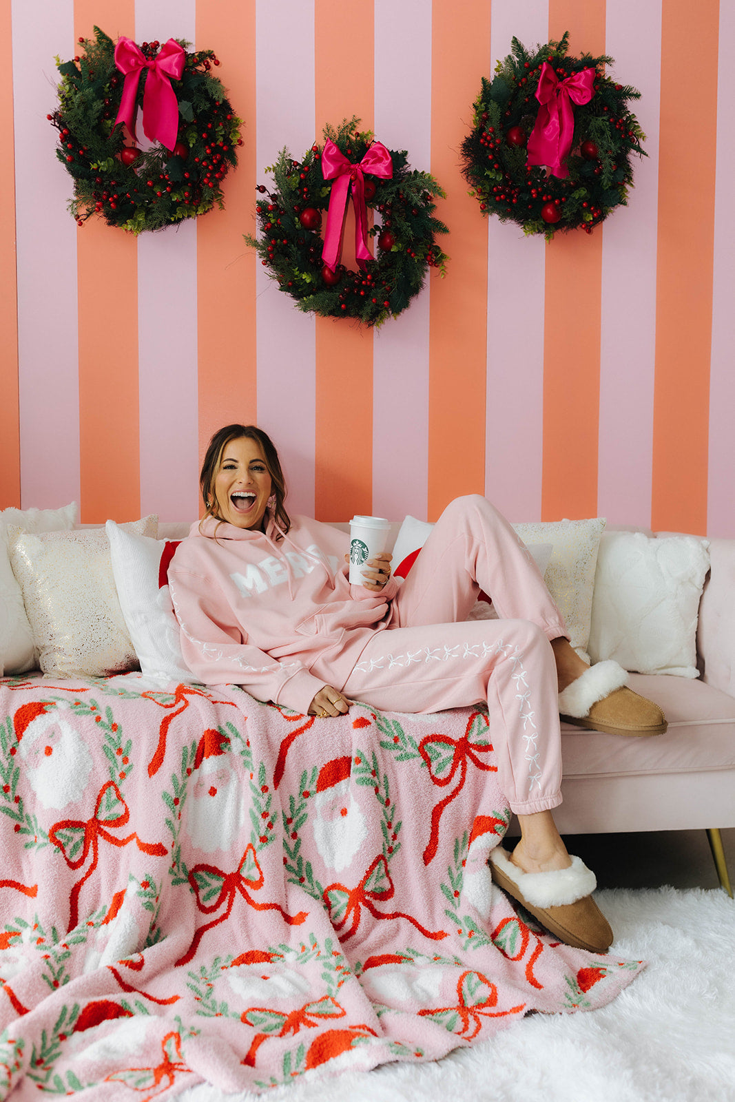 Woman sitting on a couch with a festive blanket and wreaths on a striped wall