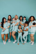Group of women and children in matching teal outfits against a teal background