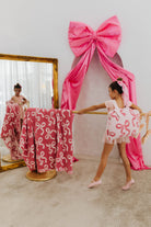 Young girl in a pink and white dress practicing ballet in front of a large pink bow decoration.