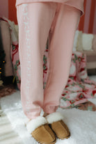 Person wearing pink sweatpants with white bows and brown slippers indoors.
