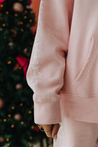 Person wearing a pink outfit with white bow details in front of a decorated Christmas tree.