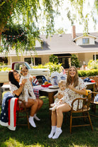 Two women and two children sitting outdoors with a house and trees in the background