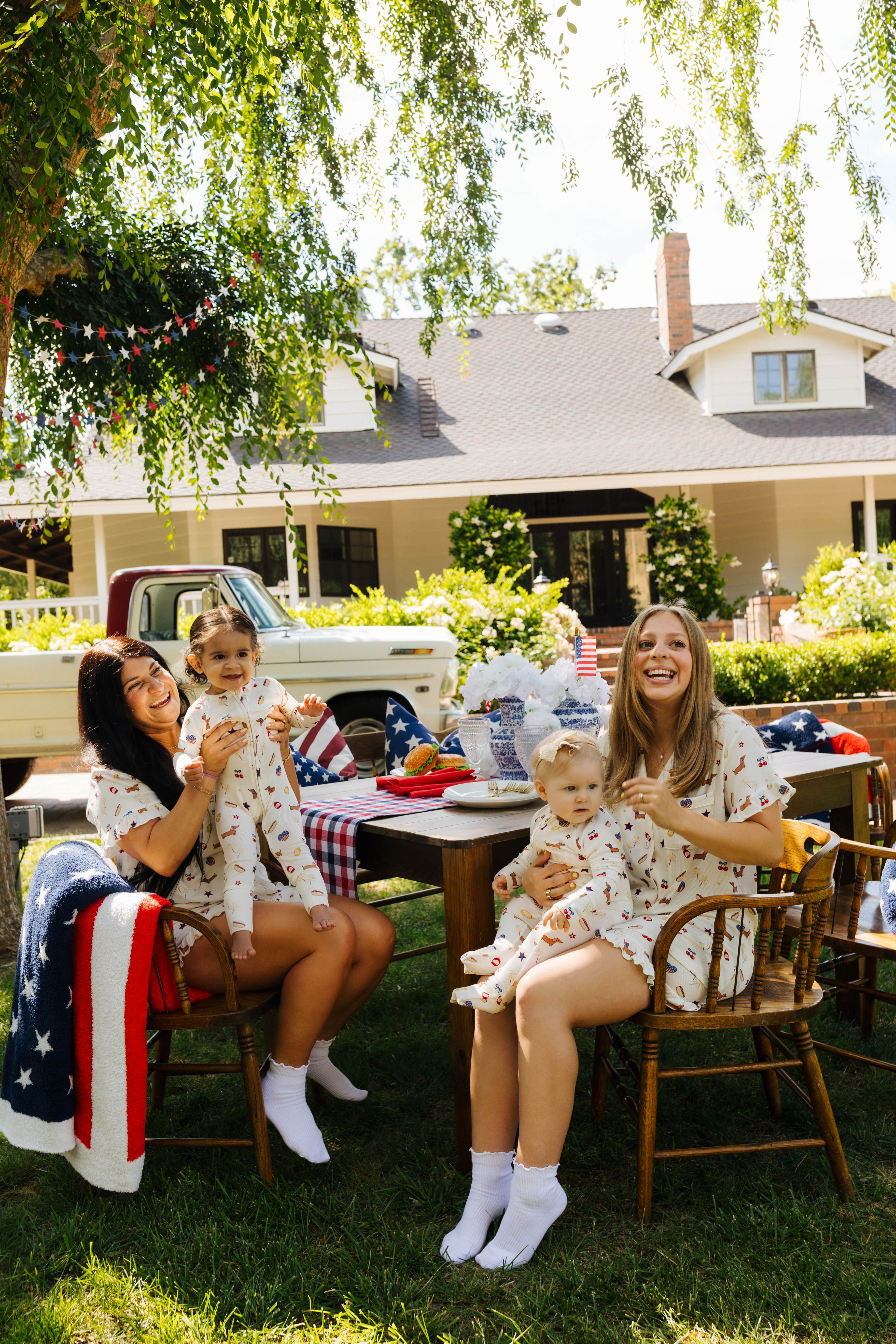 Two women and two children sitting outdoors with a house and trees in the background