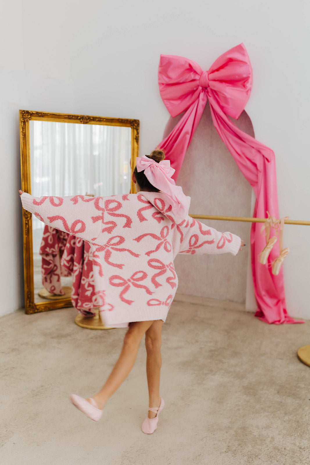 Person wearing a pink robe with pink bows in front of a large mirror and pink bow
