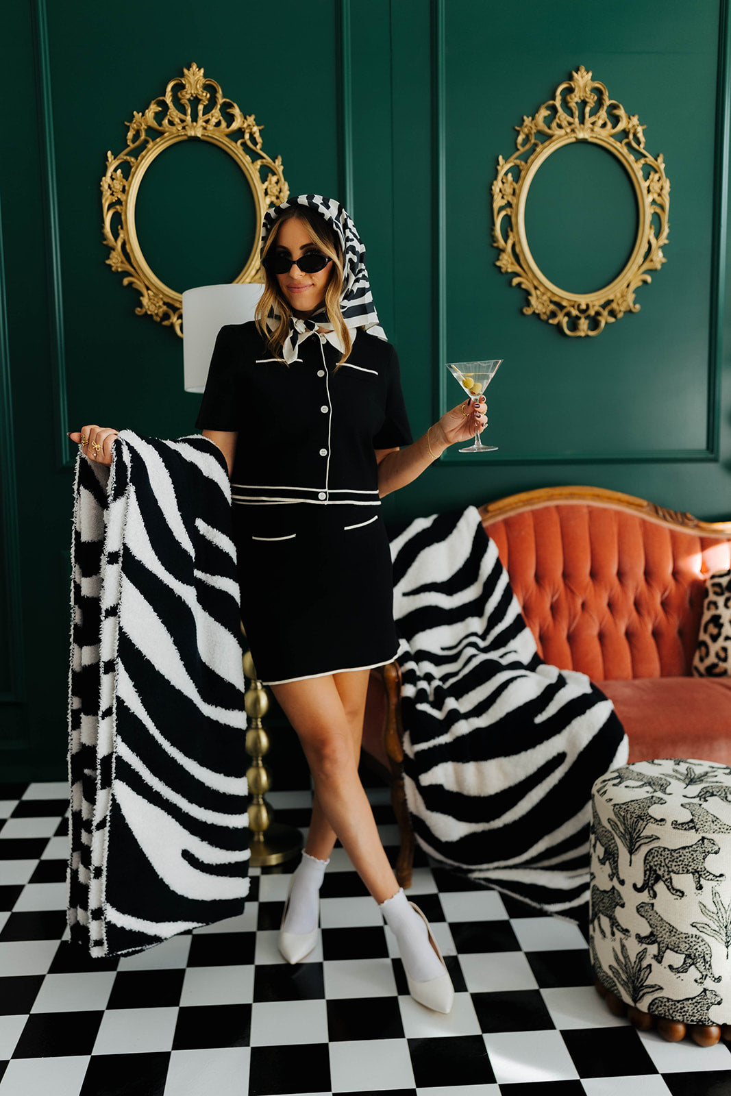 Woman in a stylish outfit with zebra pattern blanket in a room with green walls and checkered floor.