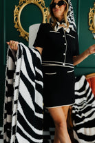 Woman holding a black and white striped blanket in front of a decorative mirror with gold frame.