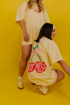 Two people wearing oversized t-shirts with graphic designs on a yellow background