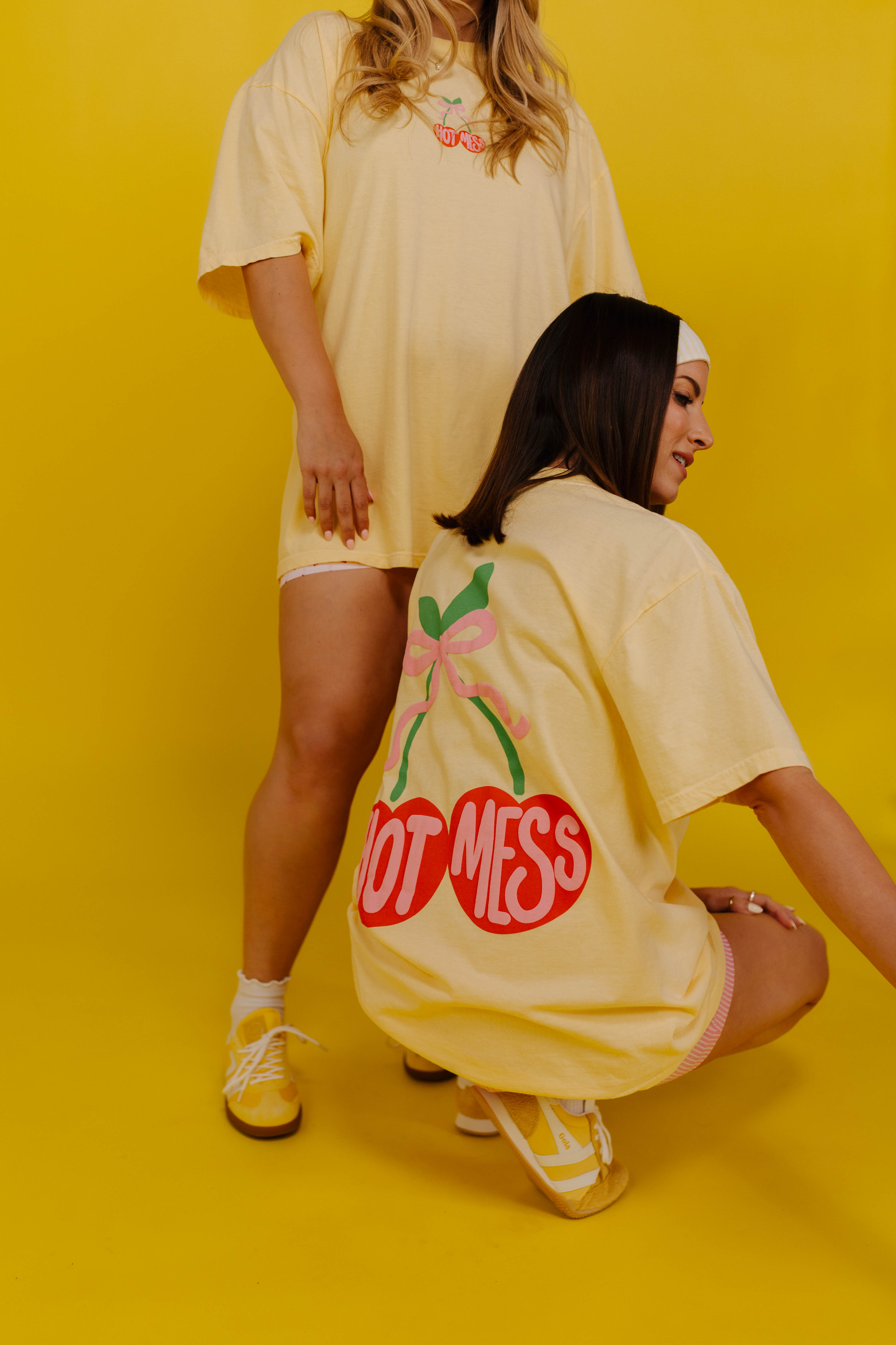 Two people wearing oversized t-shirts with graphic designs on a yellow background