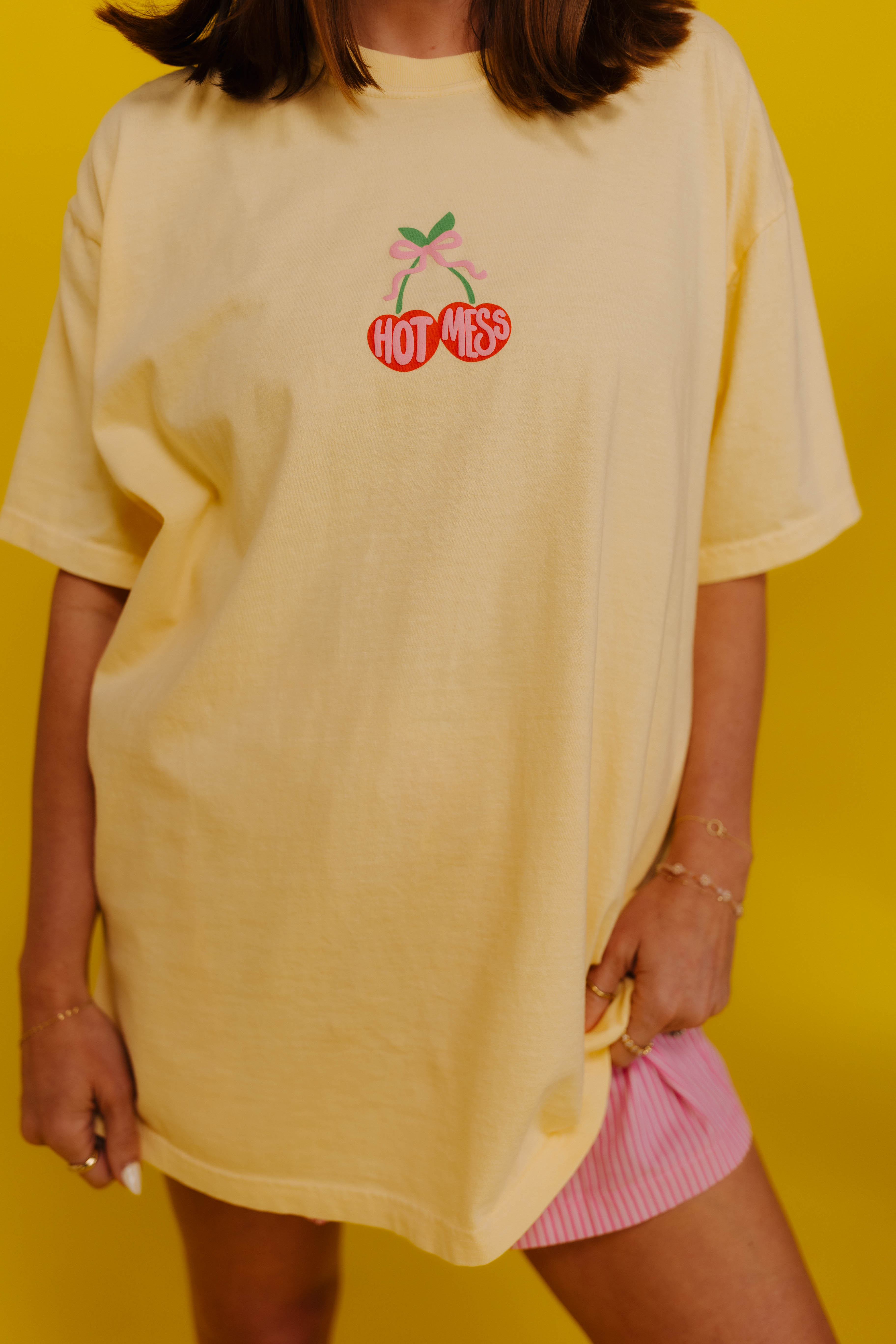 Person wearing a yellow oversized t-shirt with a logo on a yellow background