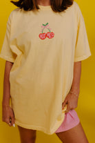 Person wearing a yellow oversized t-shirt with a logo on a yellow background