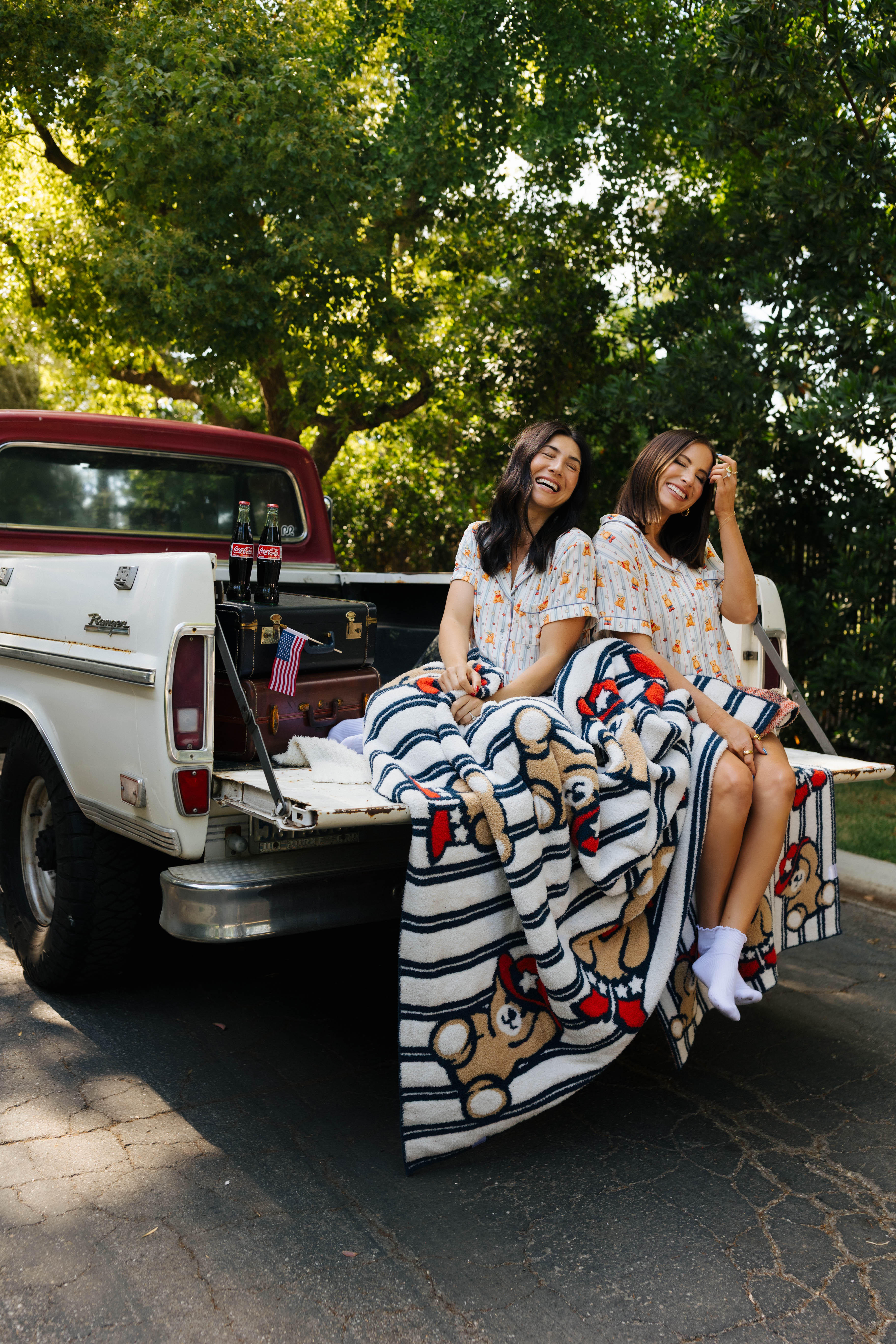 two women sitting on the back of the truck with the bear blanket over them