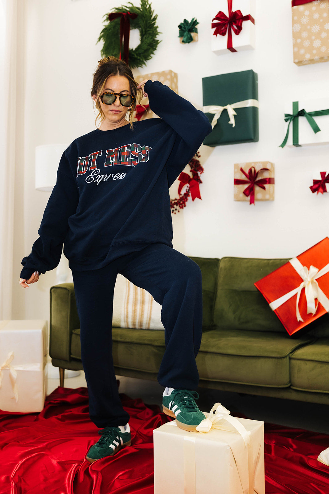 Person wearing a navy sweatshirt with text in a decorated living room with Christmas presents.