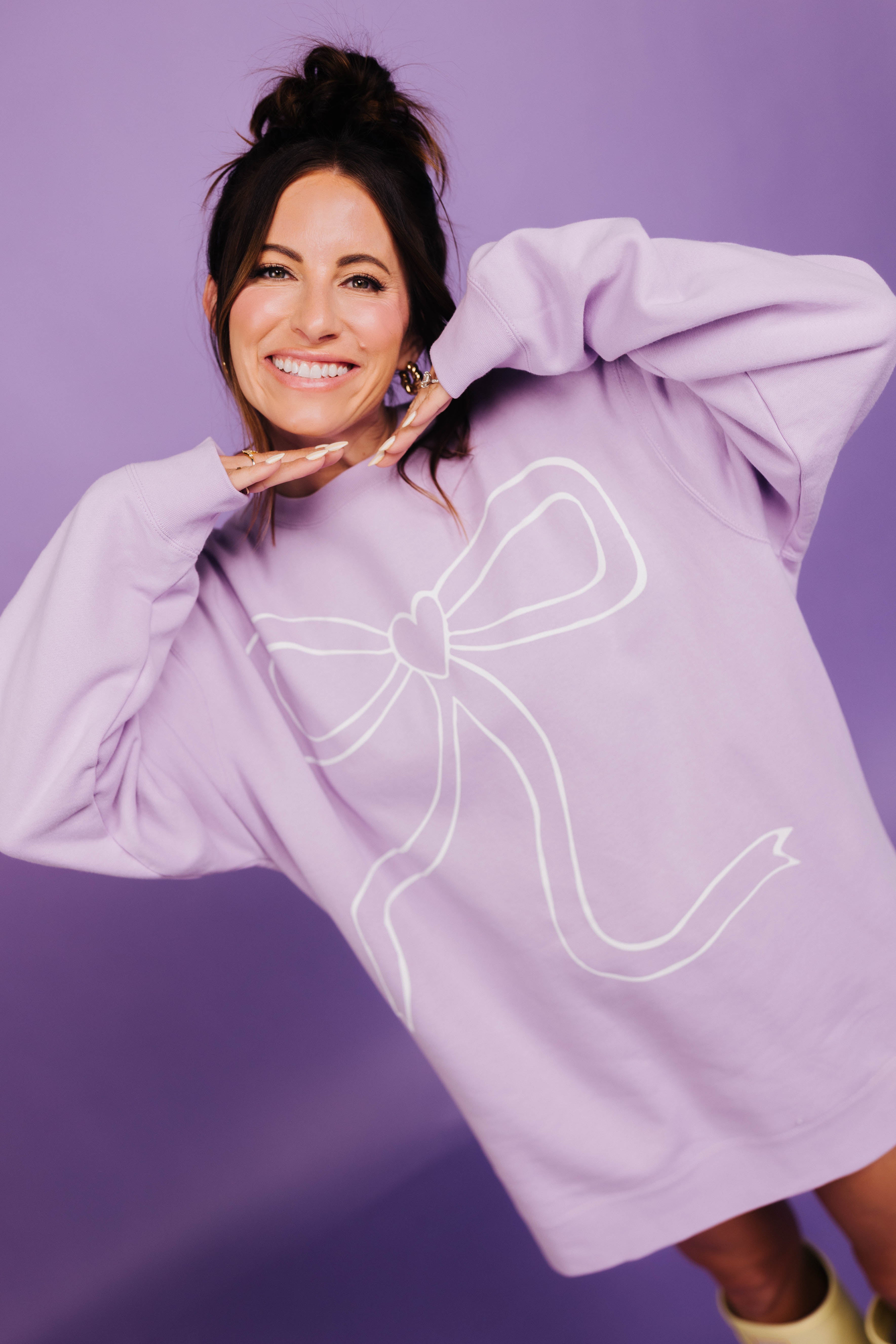 Woman wearing a light purple sweatshirt with a large white bow design on a purple background