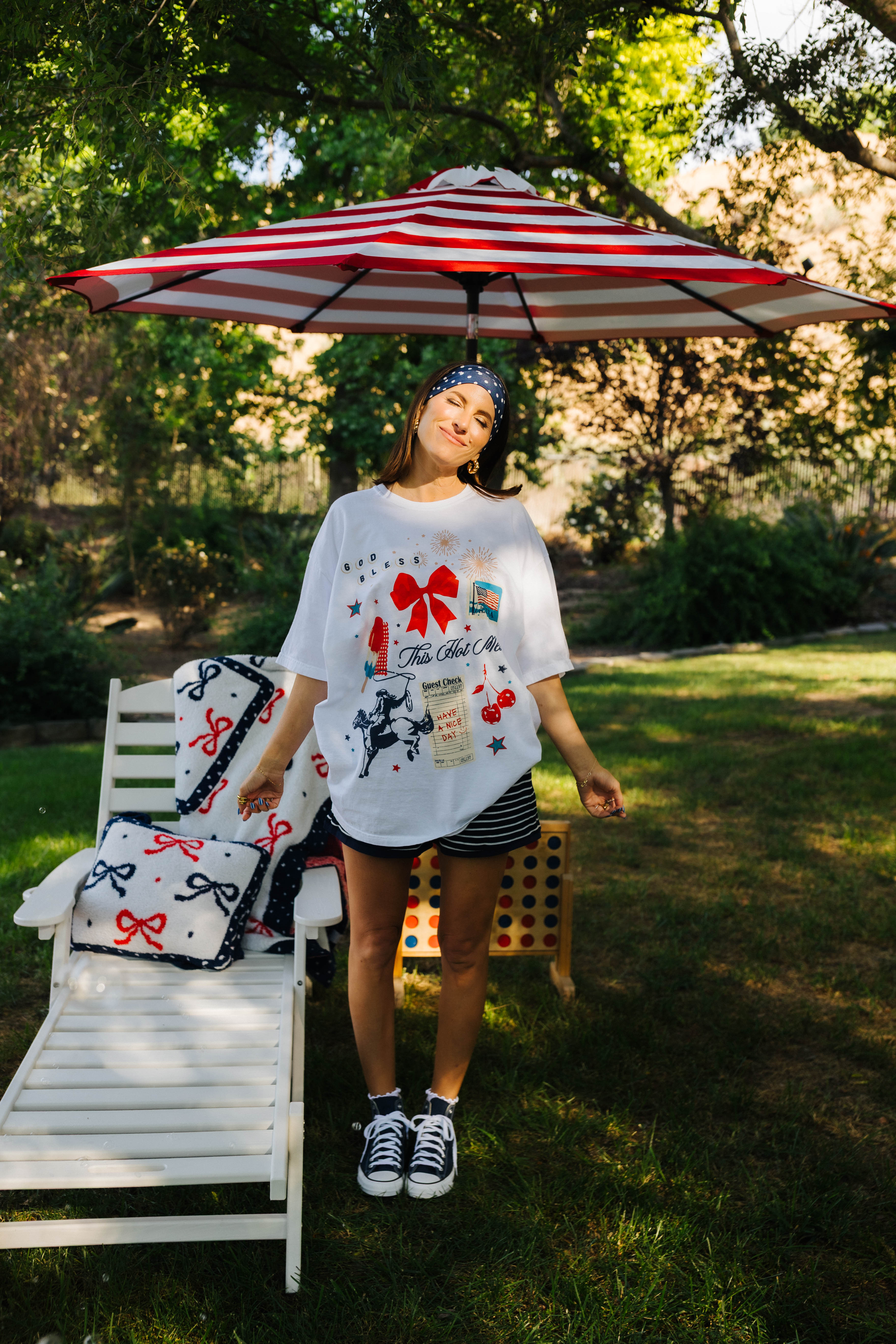 Woman standing under a red and white striped umbrella in a garden setting