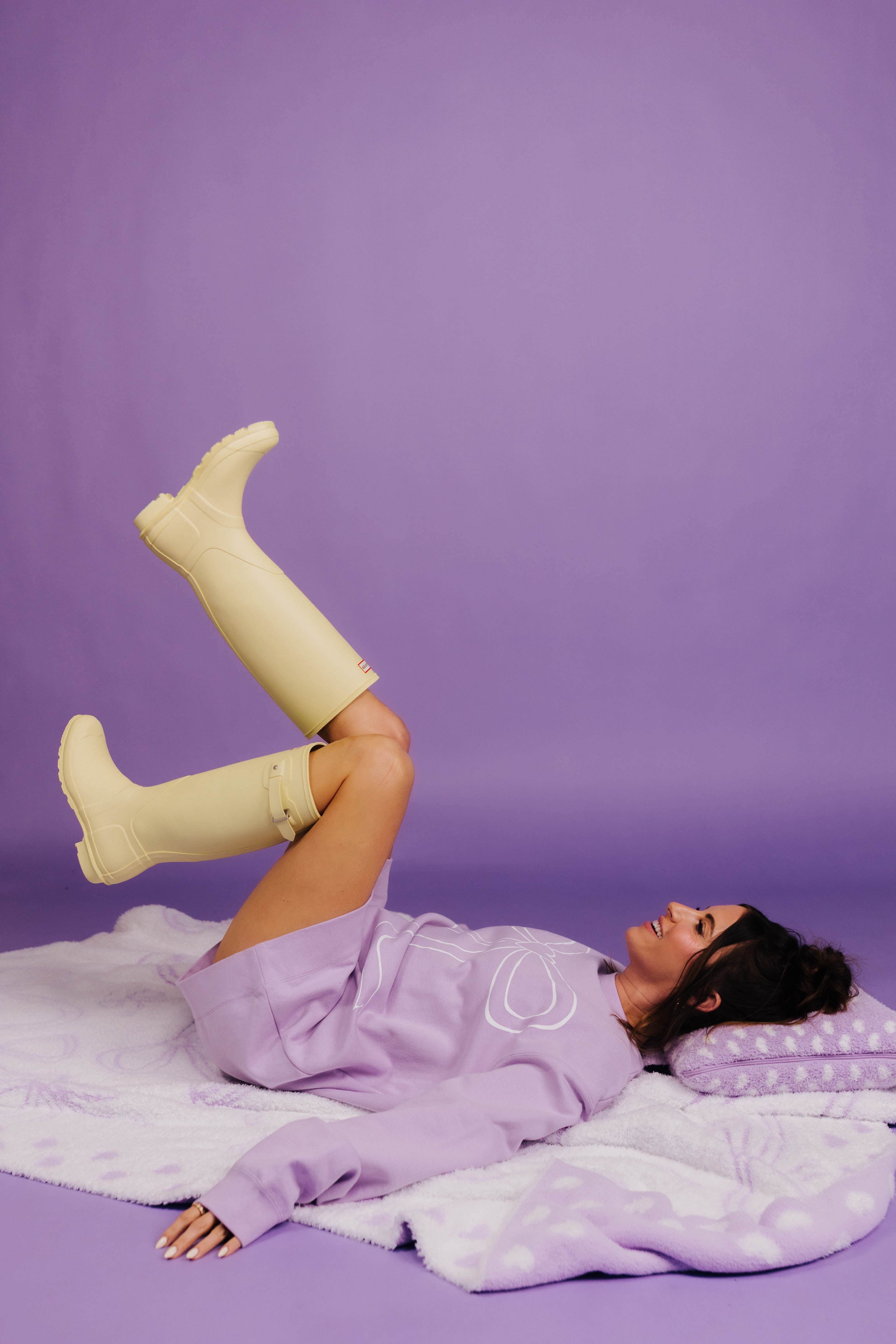 Person wearing yellow rain boots and a purple outfit on a purple background