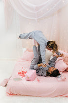 Two people in a playful pose on a bed with pink bedding and decorations.
