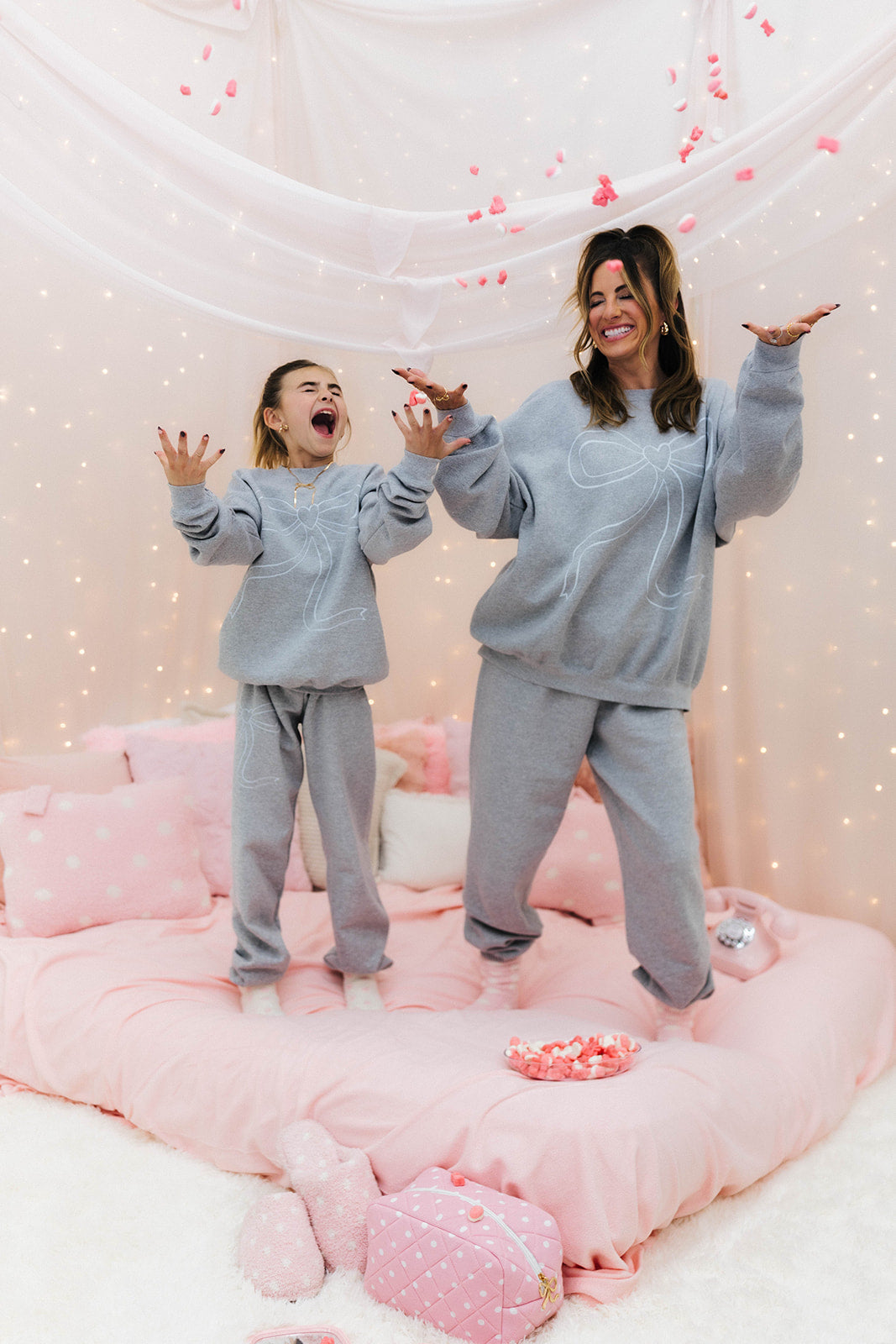 Two people in matching grey sweatsuits on a pink cushioned floor with a soft pink background.
