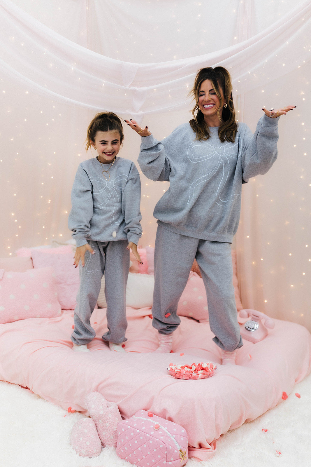Two people in matching gray outfits standing on a pink cushioned surface with a soft, light background.