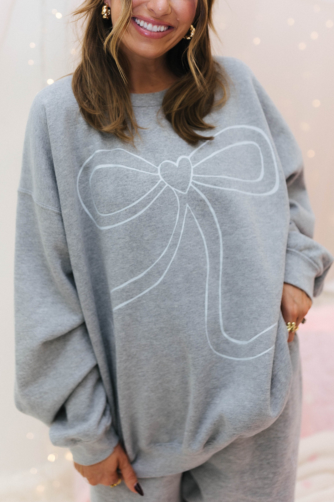Person wearing a grey sweatshirt with a large white bow design on a light pink background