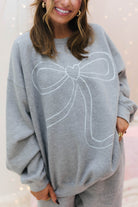 Person wearing a grey sweatshirt with a large white bow design on a light pink background