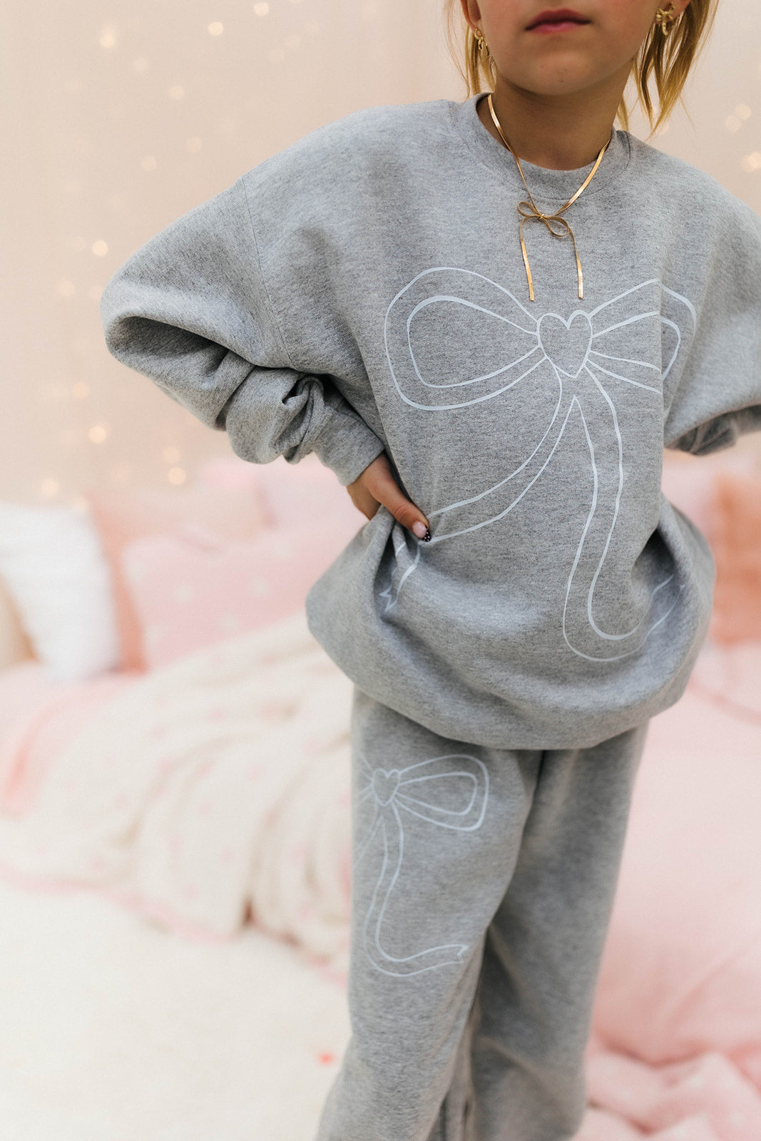 Child wearing a gray sweatshirt with a bow design on a soft pink background