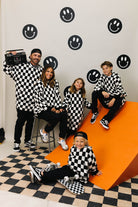 Family of five wearing checkered outfits posing on an orange and black checkered floor with smiley face decorations.