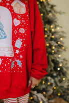 Red hoodie with festive designs worn by a person, Christmas tree in the background