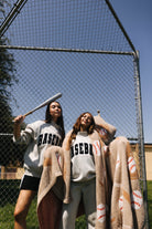 two girls posing in front of the baseball fence one holding a bat on her head and the other with a baseball blanket wrapped around her