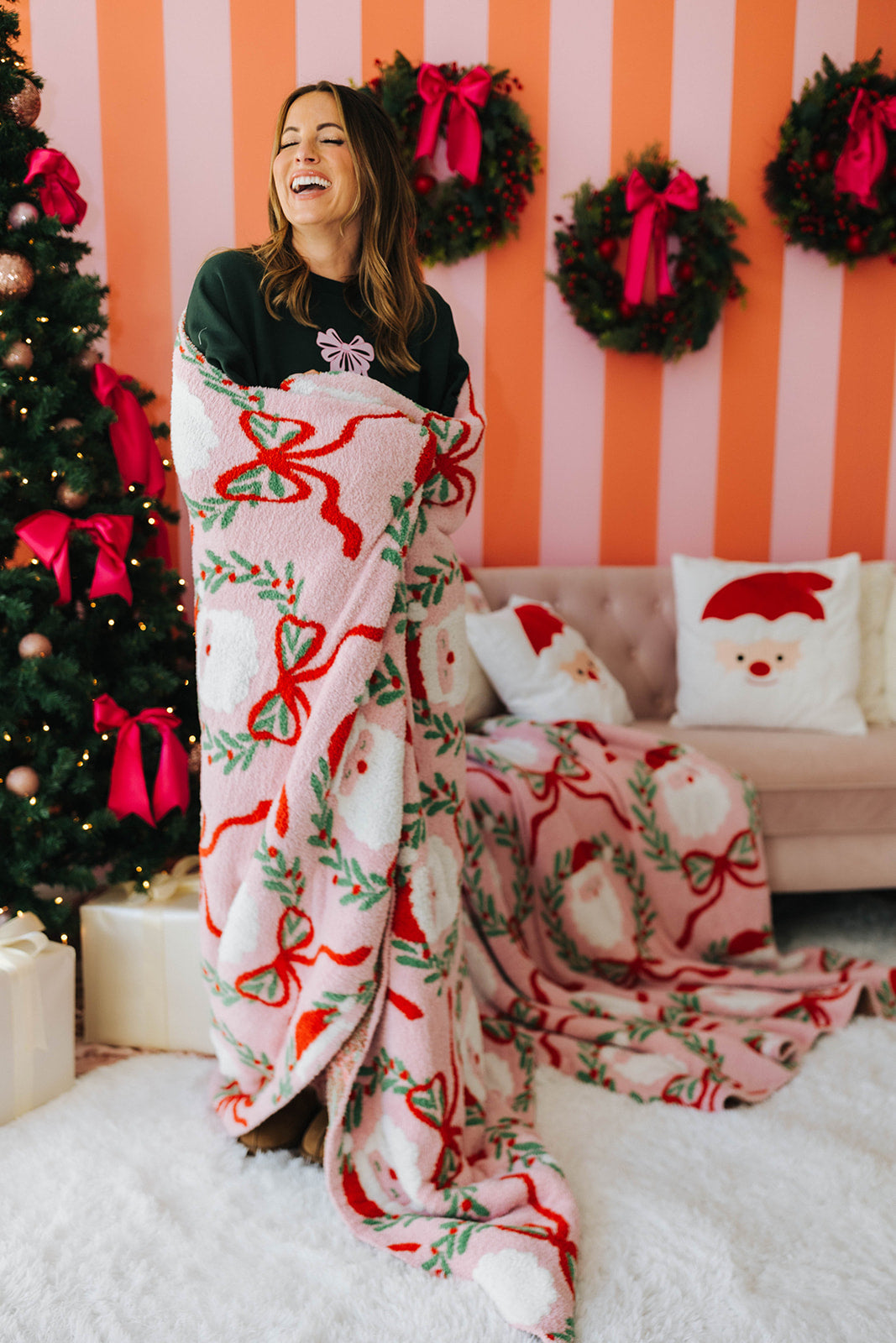 Woman wrapped in a Christmas-themed blanket in a festive room with a tree and wreaths.