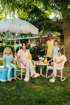 Family of five sitting outdoors under a large umbrella with a garden setting.