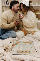 Man and woman sitting on a couch with a Scrabble board game in front of them.