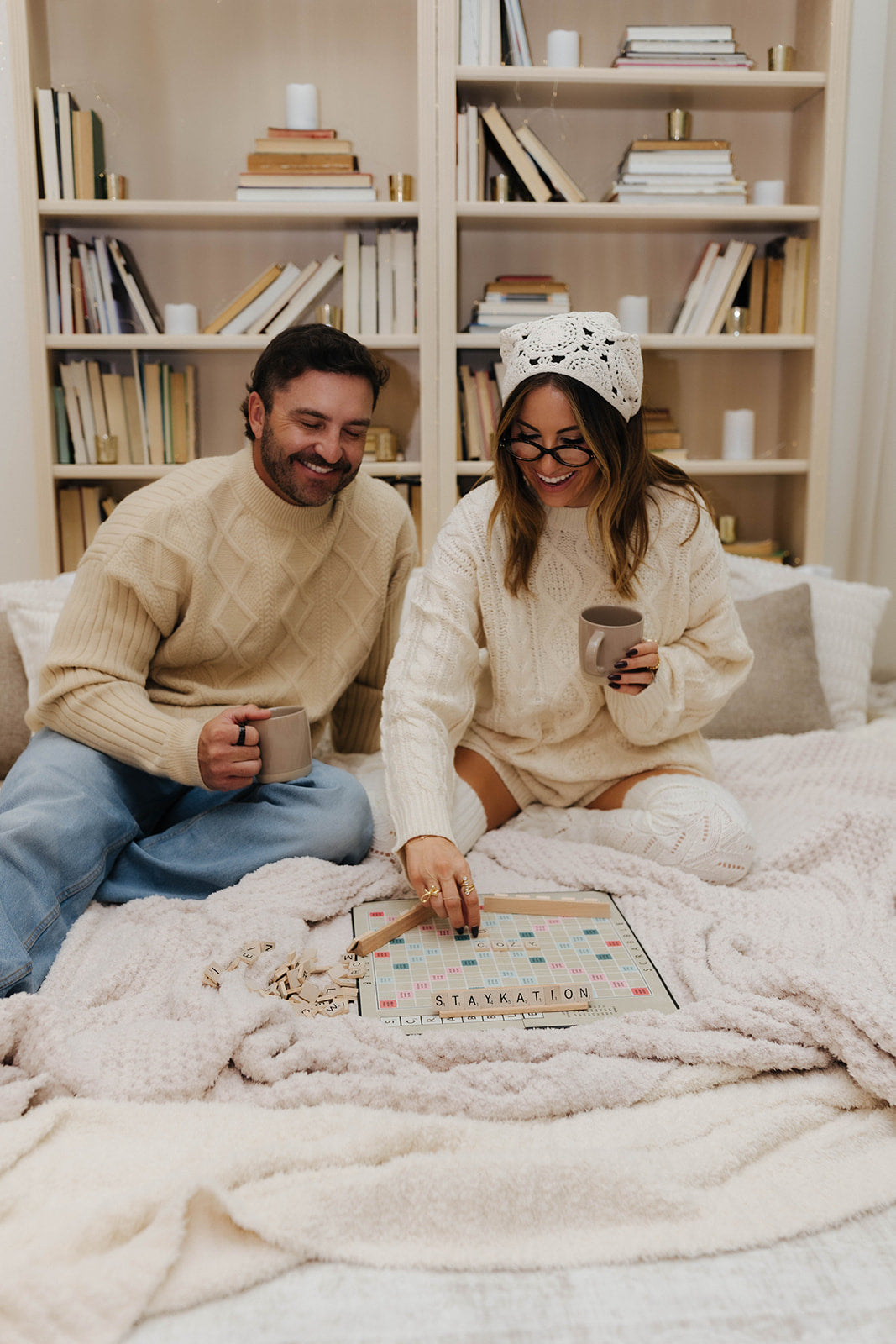 Man and woman sitting on blankets playing a board game together, surrounded by books on shelves.