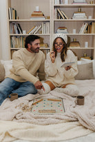 Man and woman sitting on a bed with a blanket, surrounded by books and a tablet.