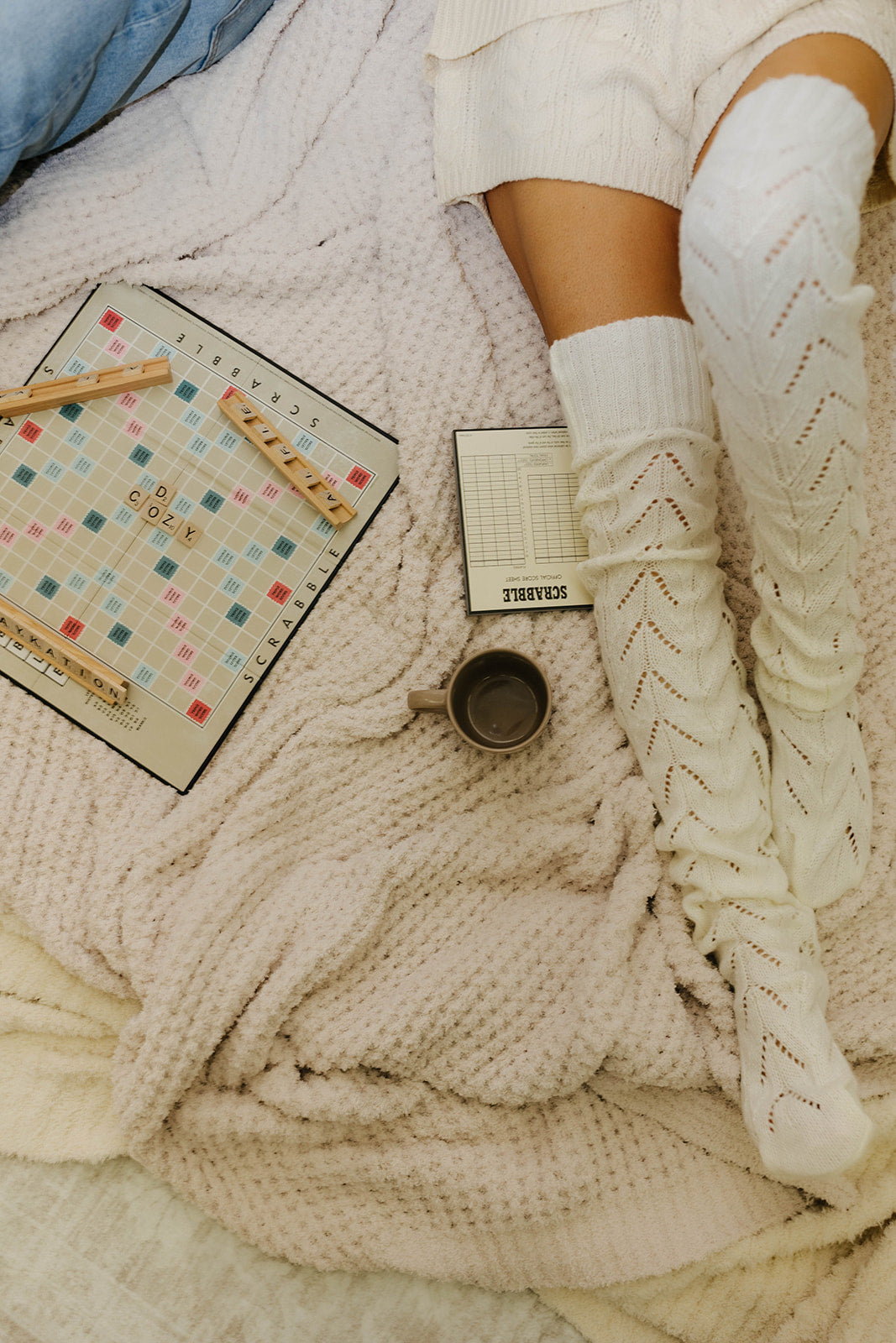 Person wearing white socks with a pattern, lying on a soft surface with a book and mug beside them.