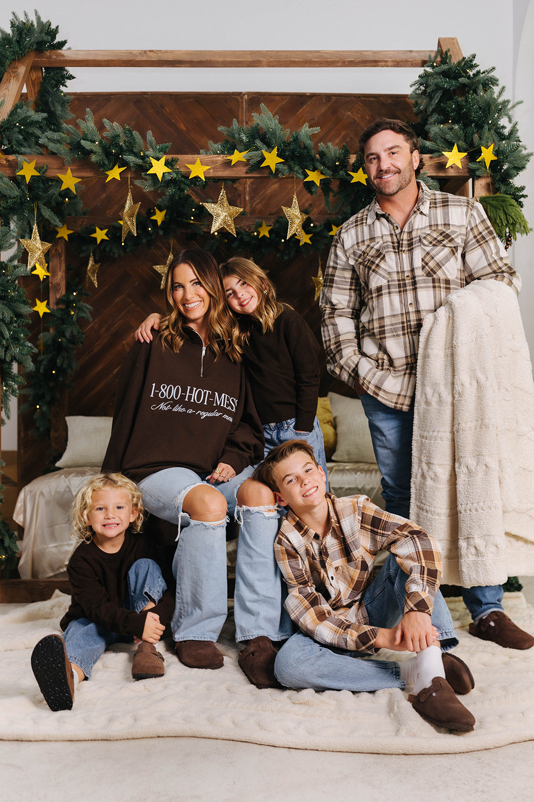Family of five posing in front of a decorated Christmas backdrop with greenery and stars.