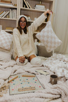 Woman in a cozy room with books and pillows, holding a pillow.
