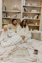 Two people sitting on a couch under a blanket with a bookshelf in the background