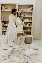 Couple in a cozy bedroom with a blanket and books on shelves.