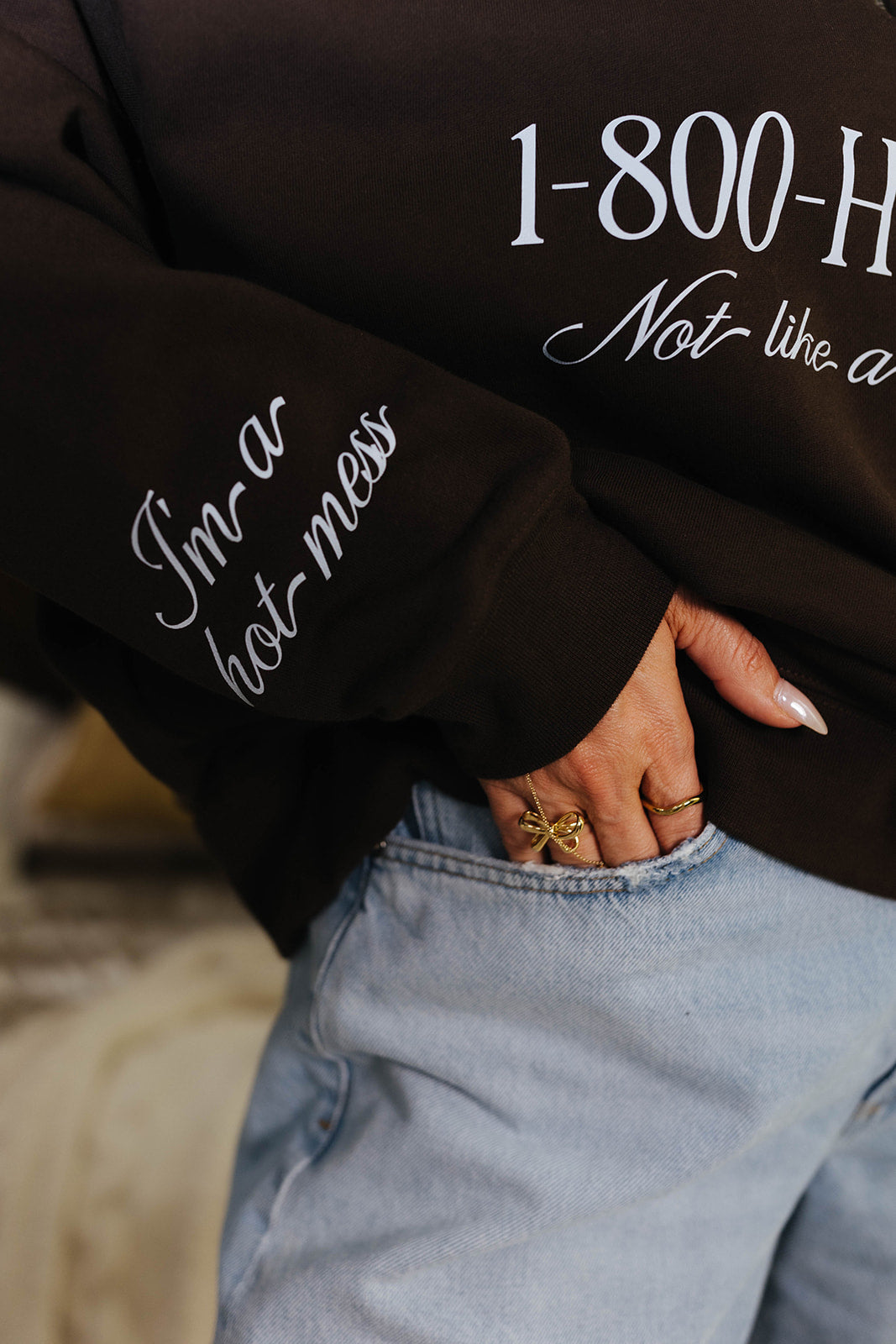 Brown sweatshirt with text and denim jeans worn by a person.