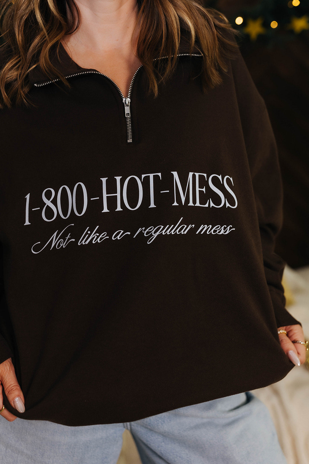 Brown sweatshirt with '1-800-HOT-MESS Not like a regular mess' text worn by a person.