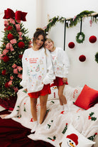 Two people in matching Christmas-themed pajamas standing in front of a decorated Christmas tree.