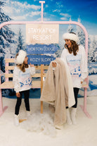 Two people in winter attire standing next to a pink chair with a 'Staycation Resort' sign in a snowy landscape.