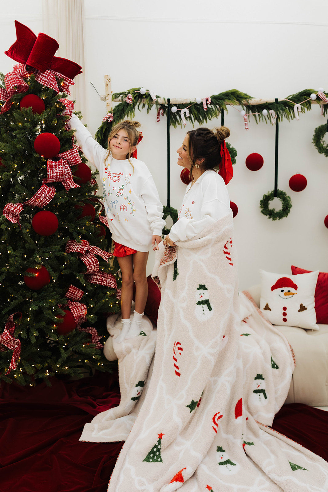 Woman and child in matching Christmas-themed outfits standing in front of a decorated Christmas tree.
